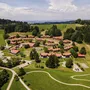 Luftaufnahme einer ländlichen Wohnsiedlung mit roten Dächern umgeben von Wiesen und Bäumen.
