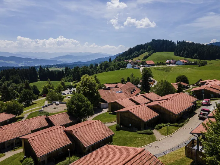 Ferienhäuser in grüner Hügellandschaft mit Bergen im Hintergrund.