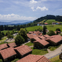 Ferienhäuser in grüner Hügellandschaft mit Bergen im Hintergrund.