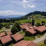 Ferienhäuser in grüner Hügellandschaft mit Bergen im Hintergrund.