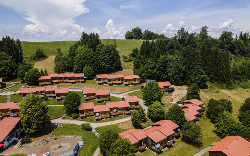 Luftaufnahme einer Siedlung mit roten Dächern, umgeben von Bäumen und Hügeln.