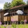 Holzgebäude mit Balkonen und Sonnenschirmen, umgeben von blühenden Pflanzen.