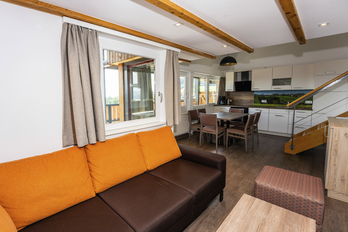 Wohnbereich mit Sofa, Tisch, Küche und Treppe in modernem Design.