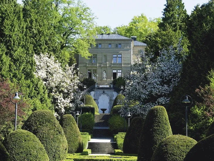 Villa Alwind in Lindau, umgeben von gepflegten Gärten und blühenden Bäumen.
