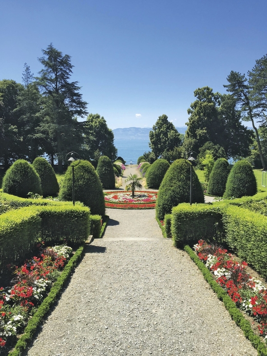 Grünanlage mit Blumenbeeten und Blick auf einen See im Hintergrund.