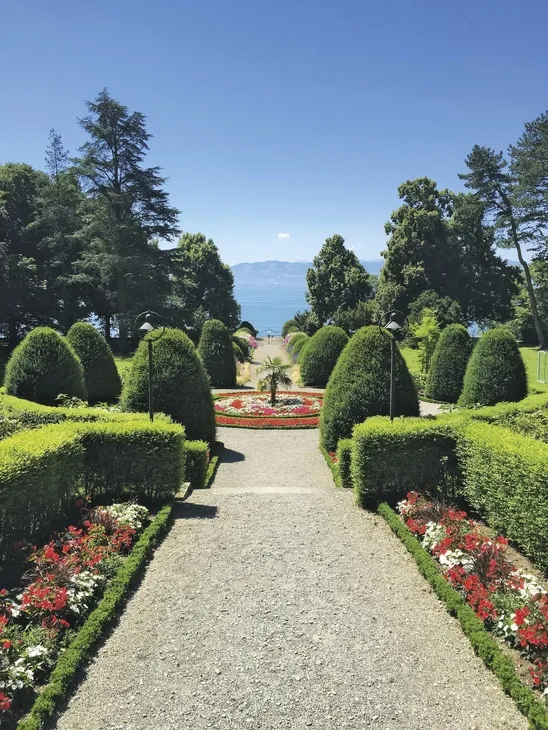 Grünanlage mit Blumenbeeten und Blick auf einen See im Hintergrund.