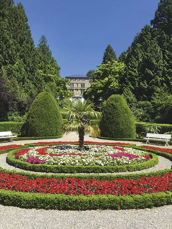 Gepflegter Park mit rundem Blumenbeet und Palmen in sonniger Umgebung.
