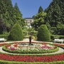 Gepflegter Park mit rundem Blumenbeet und Palmen in sonniger Umgebung.