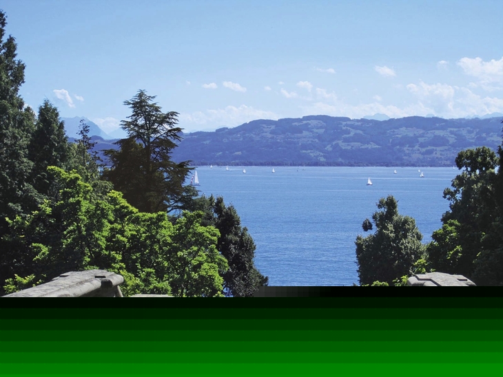 Blick von Treppe auf Bodensee mit Segelbooten und Bergen im Hintergrund.