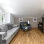 Wohnzimmer mit grauem Sofa, Sesseln und Fernseher auf Holzregal.