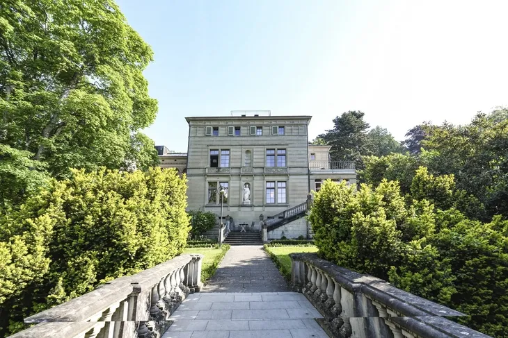Historische Villa mit Garten und Steinweg in Lindau, umgeben von Bäumen.