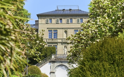 Historische Villa mit Gartenansicht, umgeben von blühenden Bäumen.