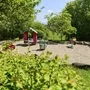 Kleiner Spielplatz mit Wiipptieren und Häuschen sowie einer Parkbank umgeben von Bäumen bei sonnigem Wetter in der Ferienanlage Lindau.