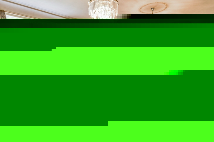 Elegantes Restaurantinterieur in der Villa Alwind in der Ferienanlage Lindau. Unterschiedlich große Holztische mit grauen, gepolsterten Stühlen auf Holzboden, sowie große weiße Fenster mit zusammengebundenen Vorhängen und moderne Kronleuchter an der Decke, die das Restaurant erhellen.