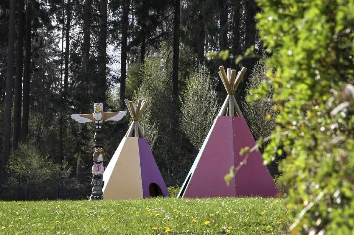Zwei bunte Tipis und ein Totempfahl auf einer Wiese im Wald der Ferienanlage Prüm.