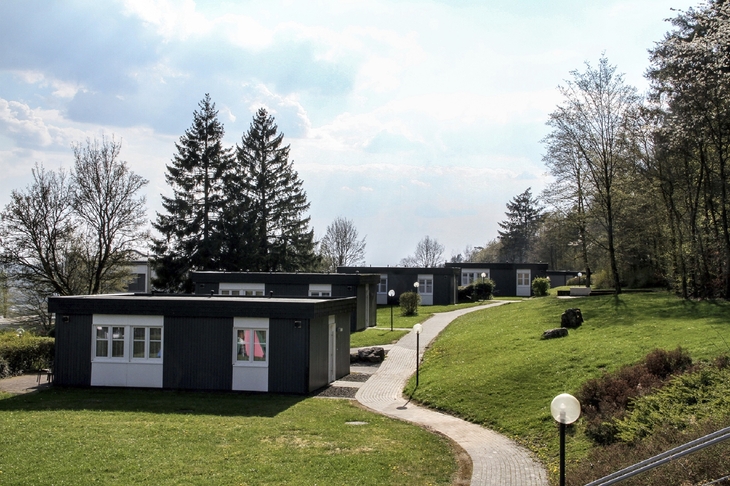 Pfad führt zu modernen Ferienhäusern der Ferienanlage Prüm in grüner, bewaldeter Landschaft.