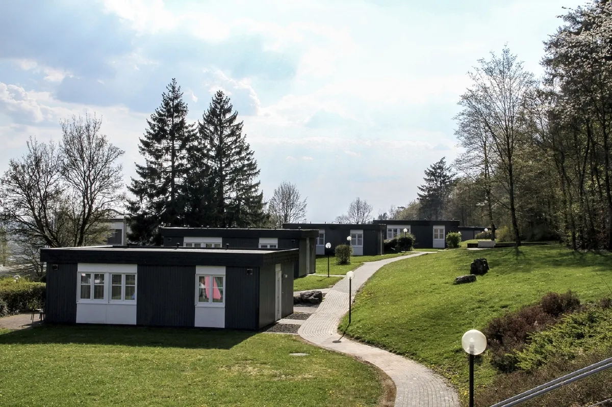 Pfad führt zu modernen Ferienhäusern der Ferienanlage Prüm in grüner, bewaldeter Landschaft.