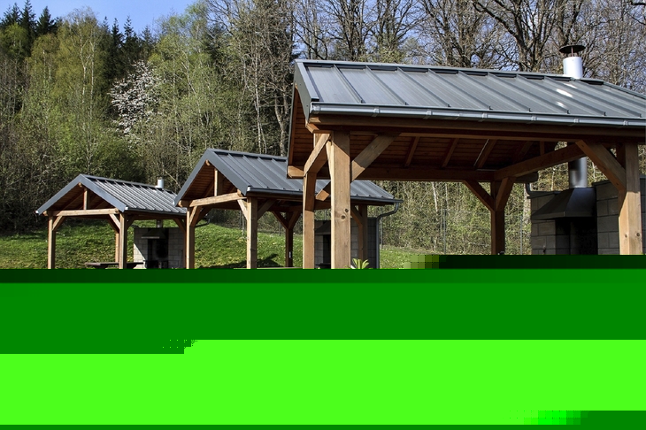 Drei überdachte Picknicktische im Freien in der Ferienanlage Prüm vor einem Waldgebiet.
