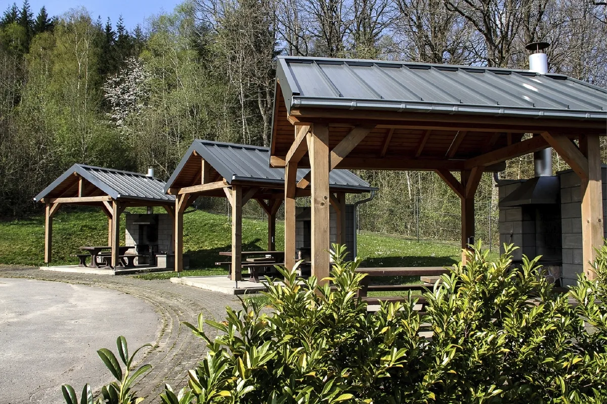 Drei überdachte Picknicktische im Freien in der Ferienanlage Prüm vor einem Waldgebiet.