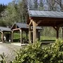 Drei überdachte Picknicktische im Freien in der Ferienanlage Prüm vor einem Waldgebiet.
