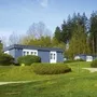 Mehrere blaue Bungalows der Ferienanlage Prüm auf einer grünen Wiese mit Wald im Hintergrund.