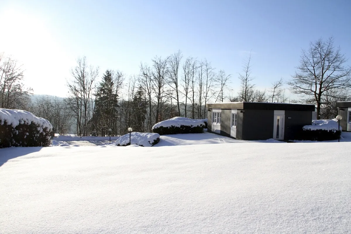 Bungalow der Ferienanlage Prüm in verschneiter Landschaft mit klarem Himmel und Bäumen im Hintergrund.
