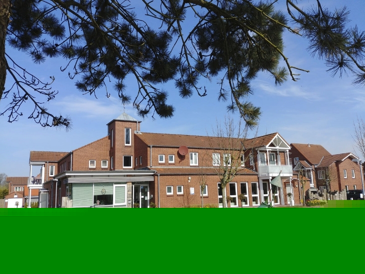 Rotes Klinkergebäude der Ferienanlage Büsum mit Parkplatz im Vordergrund bei klarem Himmel.