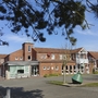 Rotes Klinkergebäude der Ferienanlage Büsum mit Parkplatz im Vordergrund bei klarem Himmel.