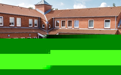 Rotes rechtwinkliges Backsteingebäude der Ferienanlage Büsum mit Terrasse, Sitzmöbeln und Sonnenschirmen bei sonnigem Wetter.