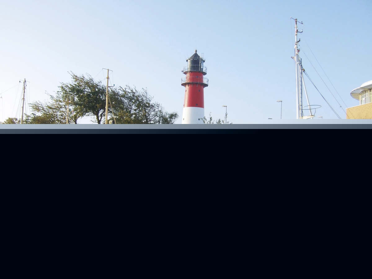 Boote im Hafen von Büsum vor einem Leuchtturm bei klarem Himmel.