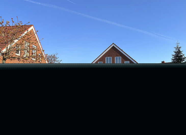Zwei Backsteingebäude, rechts die Rezeption und links das Spielhaus, mit Vorplatz der Ferienanlage Harlesiel, bei blauem Himmel.