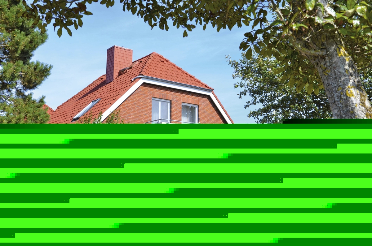 Rotes Ferienhaus mit Garten und Balkon in Ferienanlage Harlesiel, umgeben von grünen Bäumen und einem Gehweg.