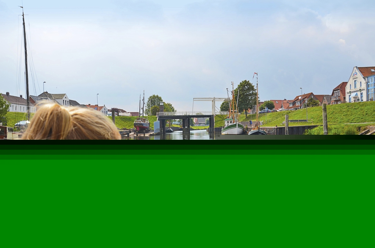 Mädchen blickt auf Wasserkanal mit Zugbrücke und Segelbooten in Harlesiel.