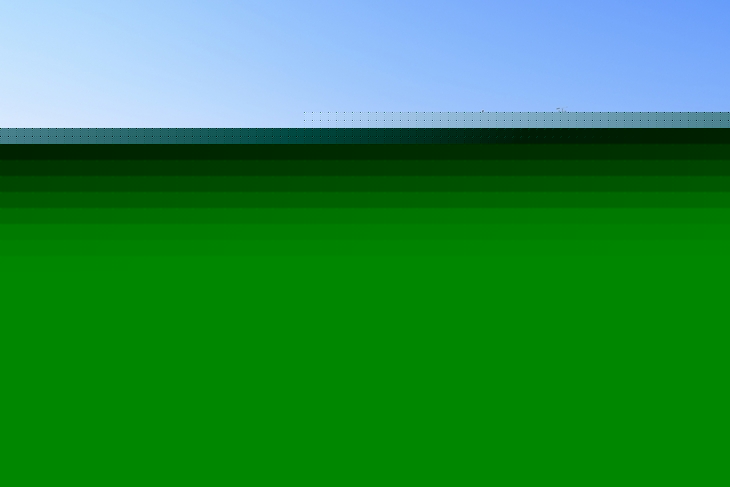 Blick auf das Meer und einen achteckigen, weißen Pavillon mit grünem Dach zu dem ein befestigter Weg hoch führt vor blauem Himmel.
