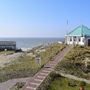 Blick auf das Meer und einen achteckigen, weißen Pavillon mit grünem Dach zu dem ein befestigter Weg hoch führt vor blauem Himmel.