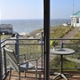 Blick vom Balkon, mit Tisch und Stuhl, der Ferienanlage Norderney auf das Meer. Rechts im Bild ein achteckige weiße Pavillon mit grünem Dach.