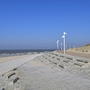 Strandpromenade mit Laternen und befestigtem Weg, mit Blick auf Meer und Strand, bei strahlend blauem Himmel.