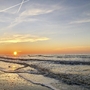 Sonnenuntergang am winterlichen Nordsee-Strand mit zarten Wellen und leicht bewölktem Himmel.