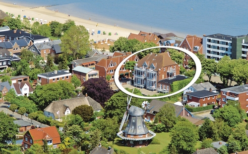 Luftaufnahme der Ferienanlage Wyk auf Föhr, umgeben von Häusern und Bäumen sowie einer Windmühle, in der Nähe des Strandes.
