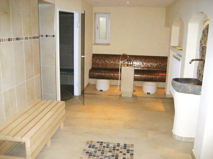 Innenraum einer Sauna mit Holzbänken und Fliesenwänden.