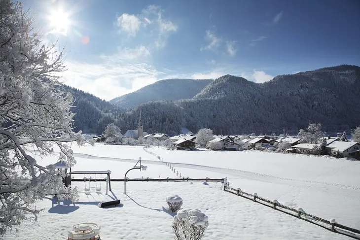 Winterlandschaft in Oberwössen mit schneebedeckten Häusern und Bergen bei Sonnenschein