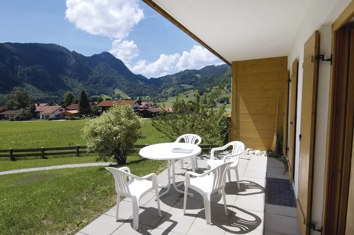 Terrasse mit weißen Stühlen und Tisch, Blick auf Berglandschaft und Dorf.