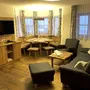 Wohnzimmer mit Sofa, Fernseher, Esstisch und Stühlen, Fenster mit Vorhängen.