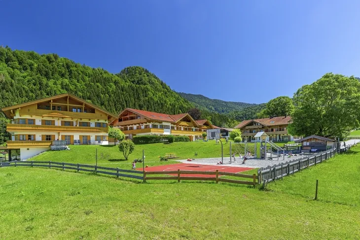 Außenansicht moderner Gebäude vor bewaldeten Bergen bei klarem Himmel.