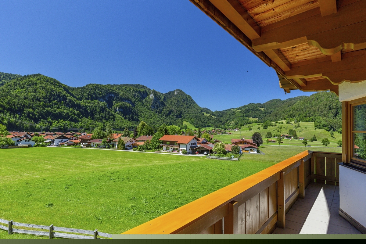 Blick vom Balkon auf eine grüne Wiese und Berge bei sonnigem Wetter.