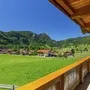 Blick vom Balkon auf eine grüne Wiese und Berge bei sonnigem Wetter.