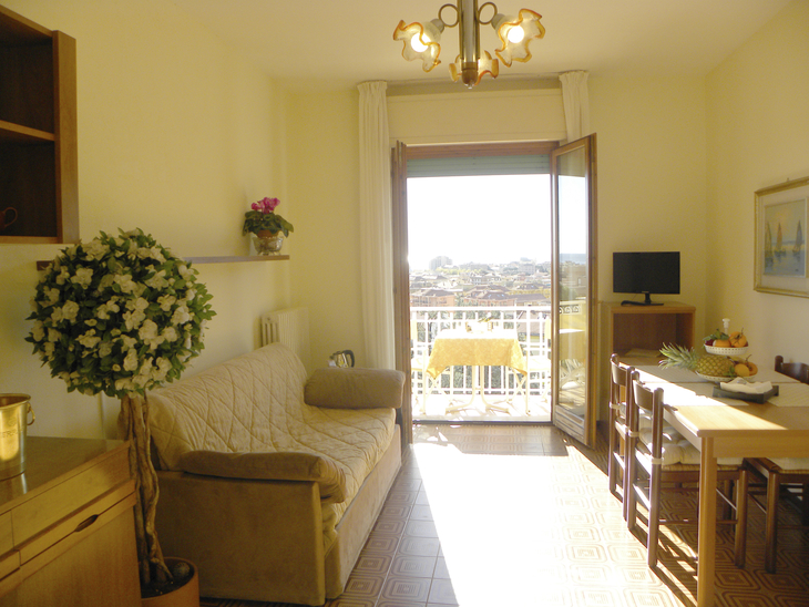 Wohnzimmer mit Sofa, Esstisch, offenem Balkon und Blick auf die Landschaft.