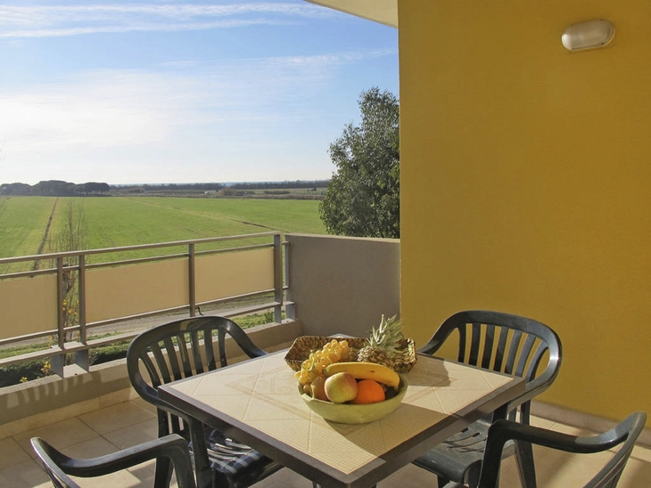 Terrasse mit Tisch, vier Stühlen und Obstschale, Blick auf Feld und blauen Himmel