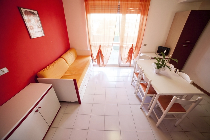 Wohnzimmer mit roter Wand, Sofa, Esstisch und großer Fensterfront.