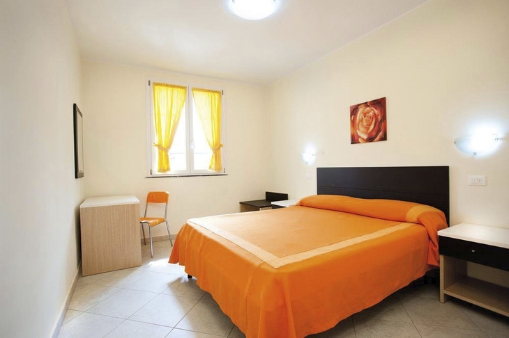 Zimmer mit orangefarbenem Bett und gelben Vorhängen.